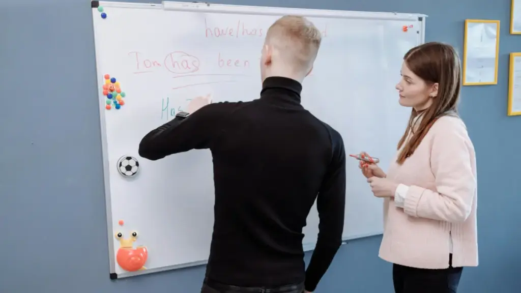 Seorang murid mengerjakan soal di papan tulis dibimbing oleh gurunya di sebelah kanan