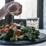 potret seseorang sedang menuangkan salad dressing ke potongan sayur