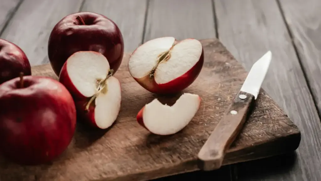 Potret potongan apel dan apel utuh ditata di atas talenan lengkap dengan pisau