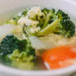 Potret semangkuk sup berisi kuah dengan potongan wortel, sawi, dan brokoli serta telur