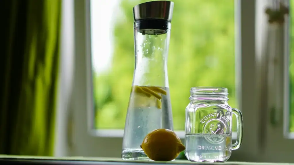 Potret sebotol infused water lemon dan gelas yang saling berdampingan di atas meja
