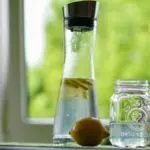 Potret sebotol infused water lemon dan gelas yang saling berdampingan di atas meja