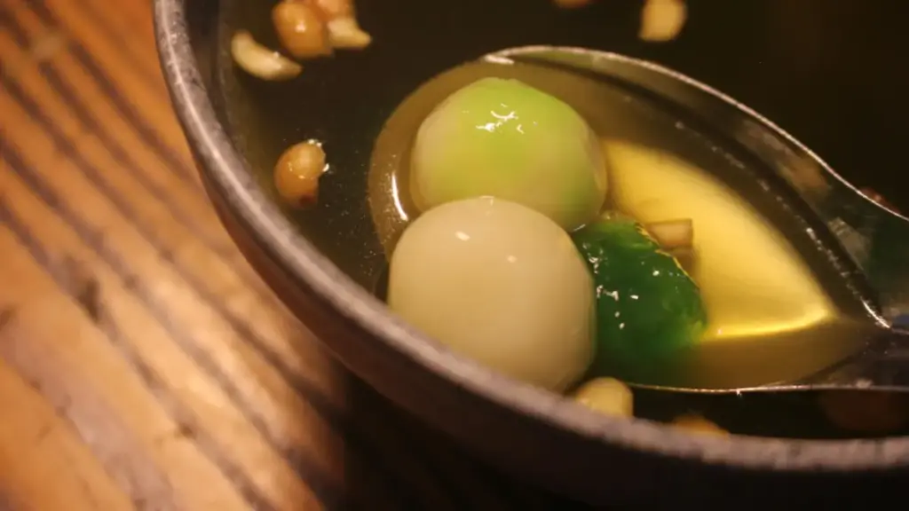 Potret semangkuk wedang ronde yang diambil dengan sendok dengan taburan kacang