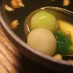 Potret semangkuk wedang ronde yang diambil dengan sendok dengan taburan kacang