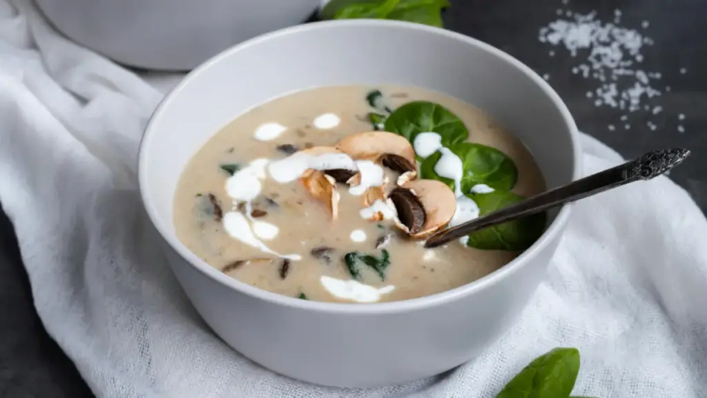 Potret semangkuk mushroom soup dengan sendok tersaji di atas serbet putih.