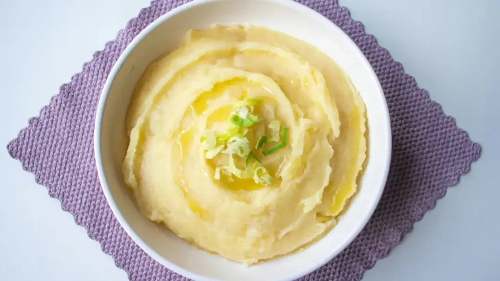 Potret semangkuk mashed potato ditaburi olive oil dan bawang daun disajikan diatas serbet ungu