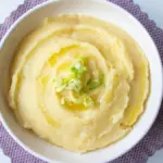 Potret semangkuk mashed potato ditaburi olive oil dan bawang daun disajikan diatas serbet ungu