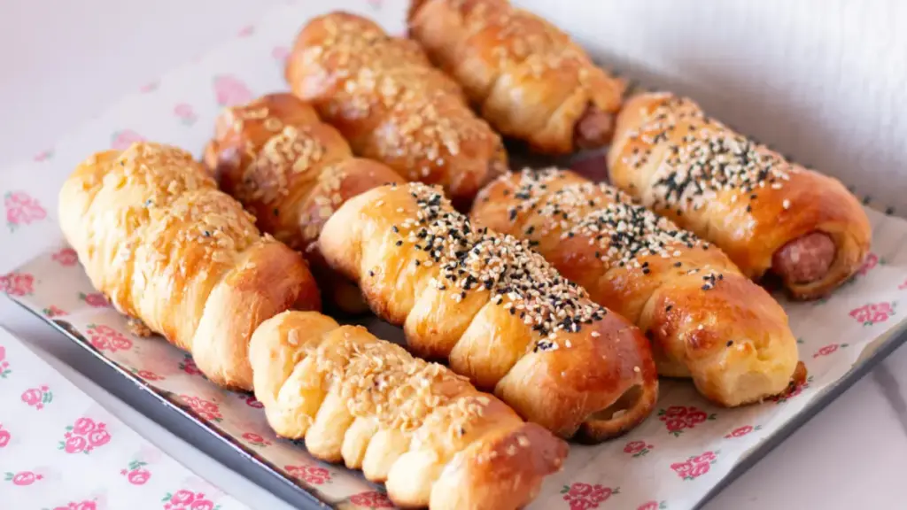 Potret sepiring puff pastry dengan isian sosis dengan topping keju dan biji wijen