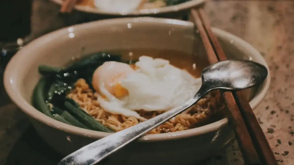 Potret semangkuk mie kuah dengan sayur dan sendok serta sumpit ditata di atasnya.
