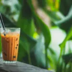 Potret segelas milk tea dengan sendok dan sedotan.