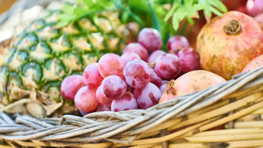 Potret sekeranjang buah anggur, nanas, dan delima.