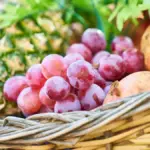 Potret sekeranjang buah anggur, nanas, dan delima.