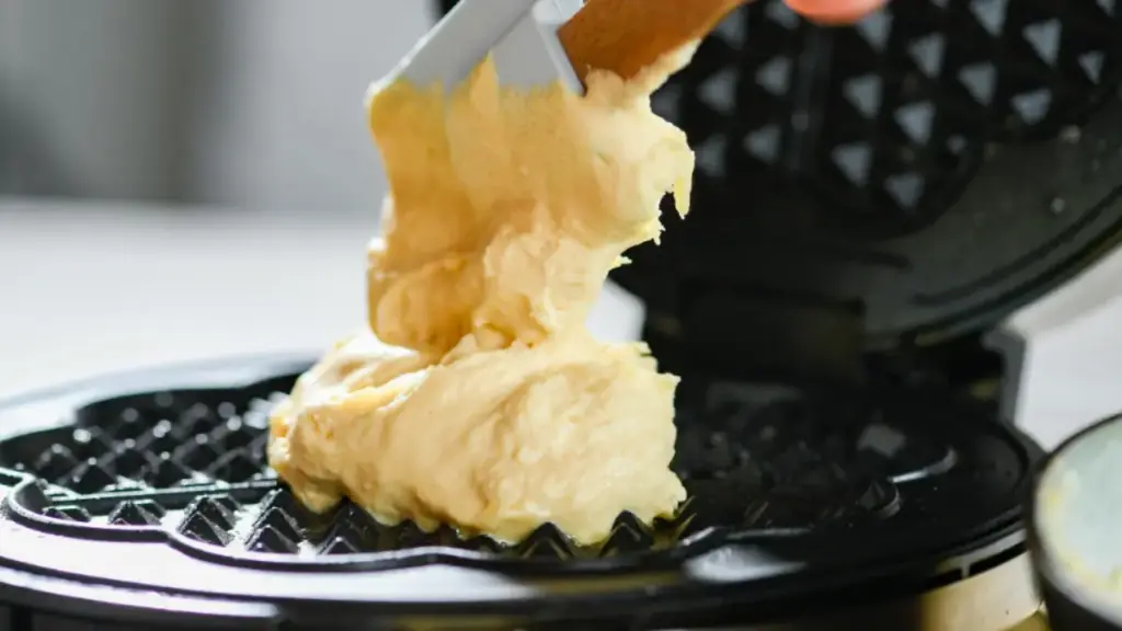Potret sesorang sedang manuangkan adonan ke cetakan waffle menggunakan spatula