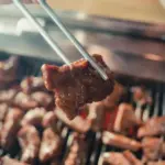 Potret sepotong dagin sapi yang dipanggang dan diambil menggunakan sumpit.