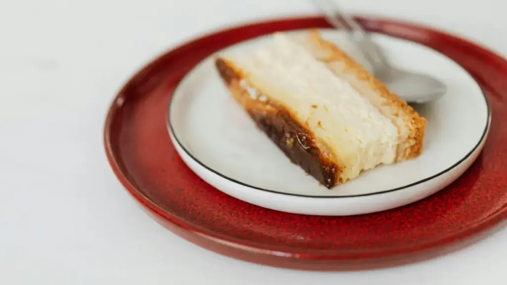 Potret sepotong cheesekace tersaji di atas piring dengan sendok di sebelah kanan