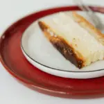 Potret sepotong cheesekace tersaji di atas piring dengan sendok di sebelah kanan