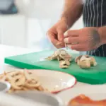 Potret seseorang sedang membersihkan jamur di atas talenan