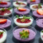Berbagai macam panna cotta terpajang rapi dengan topping krim dan stroberi.