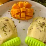 popsicle dan mangga tertata di atas piring dengan taburan kelopak bunga sebagai hiasan.