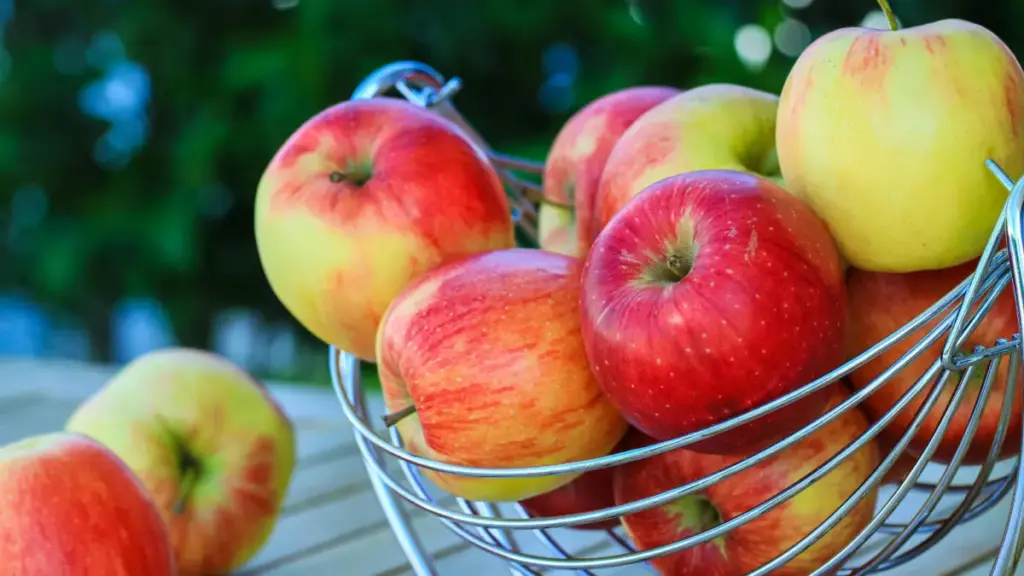 Sejumlah apel tertumpuk di dalam keranjang buah besi di luar ruangan