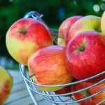 Sejumlah apel tertumpuk di dalam keranjang buah besi di luar ruangan