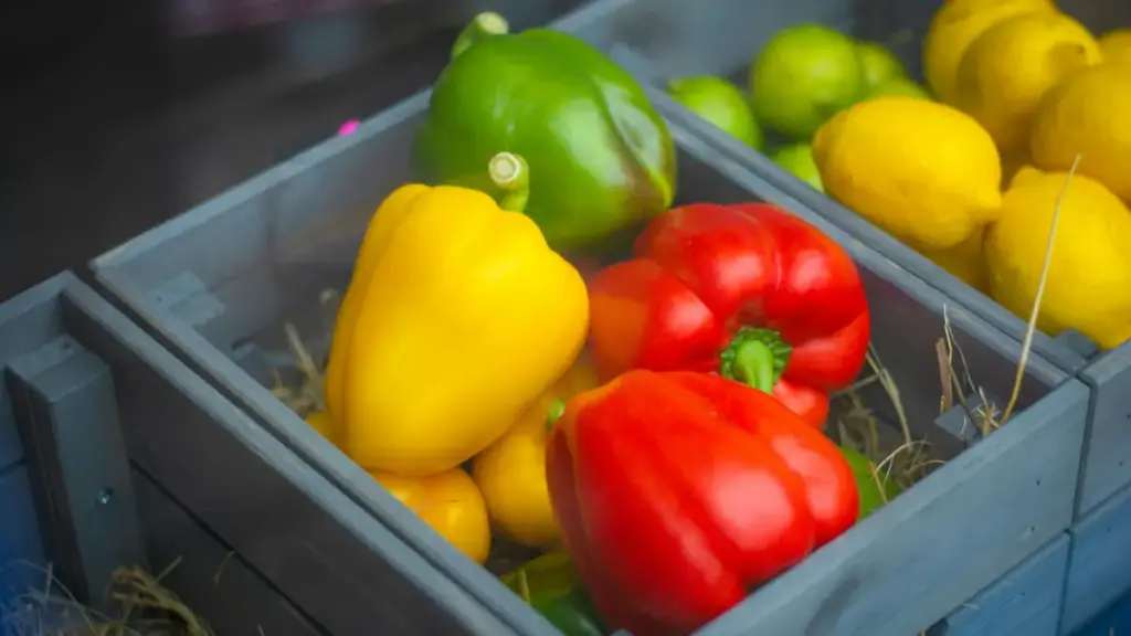 Potret setumpukan paprika merah, kuning, dan hijau di dalam keranjang kayu dengan jerami.