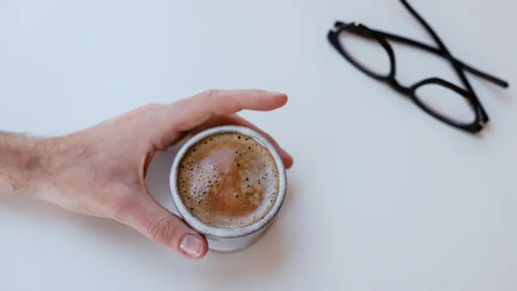 Potret seseorang memegang segelas kopi dnegan kacamata tergeletak di dekatnya