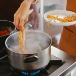 Potret sesorang memasak pasta di atas panci dan saus secara bersamaan