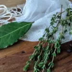 Potret bay leaf, rosemary, celery, dan black pepper tergeletak di atas meja dengan kain ikat serta tali kasur