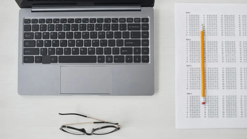 gambar berisi laptop, selembar kertas ujian dan pensil