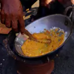 Potret seseorang sedang membuat kerak telor menggunakan tungku.