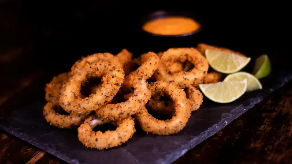 Potret sepiring onion rings tersaji di atas piring dengan hiasan potongan lemon