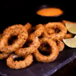 Potret sepiring onion rings tersaji di atas piring dengan hiasan potongan lemon