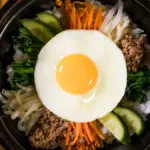 Potret semangkuk bibimbap berisi telur, daging, lobak, mentimun, wortel, dan nasi