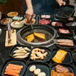 Potret seseorang memanggang daging di meja all you can eat dengan berbagai bahan makanan