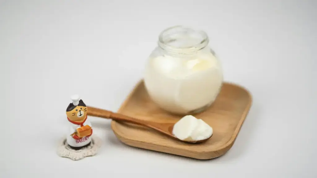 Potret segelas yogurt dengan sendok kayu dan miniatur kucing