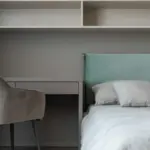 Potret pojok ruangan berisi kasur, kursi, dan rak kabinet.